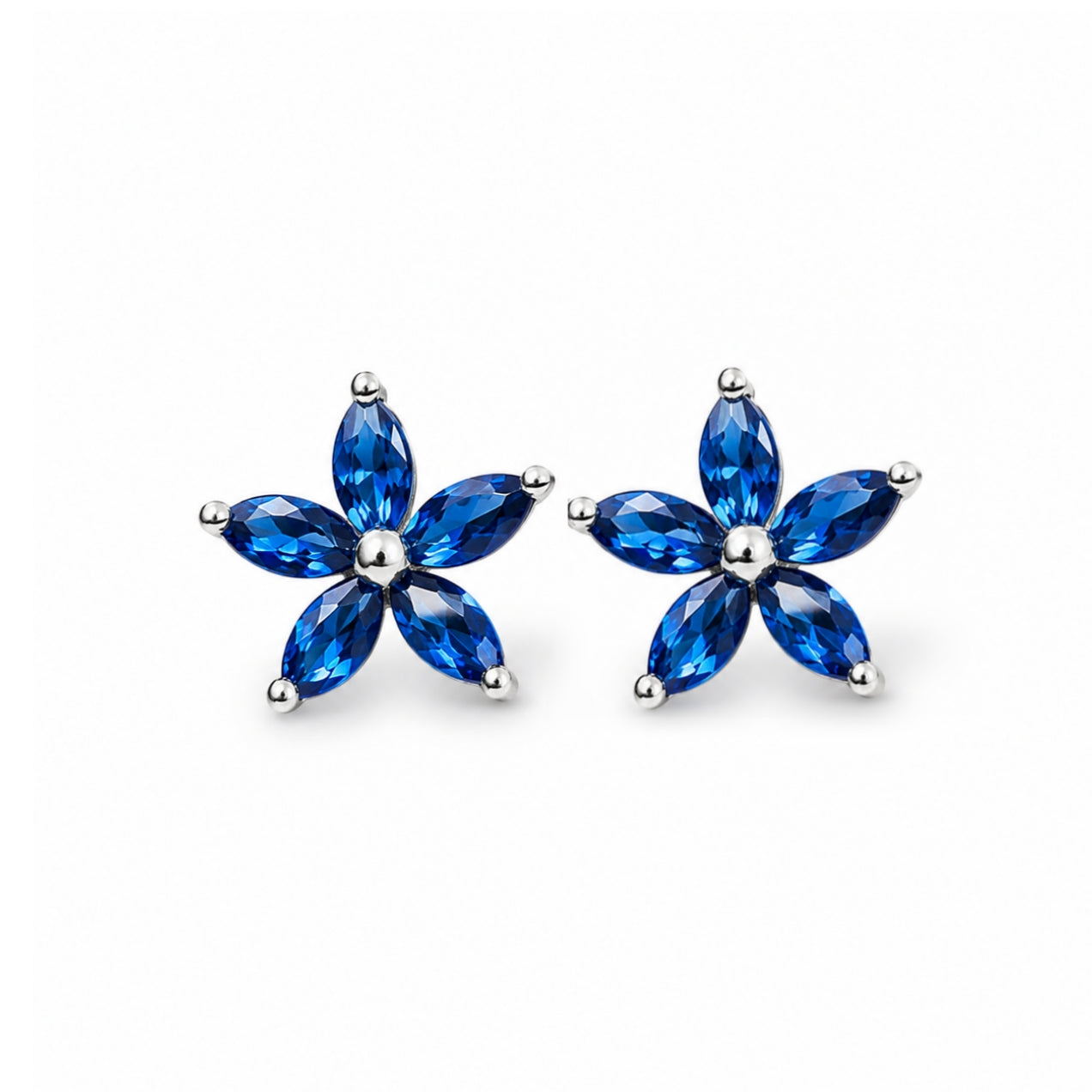 A pair of silver stud earrings shaped like small five-petal flowers, with marquise-cut blue gemstones and polished silver prongs, shown on a plain white background.