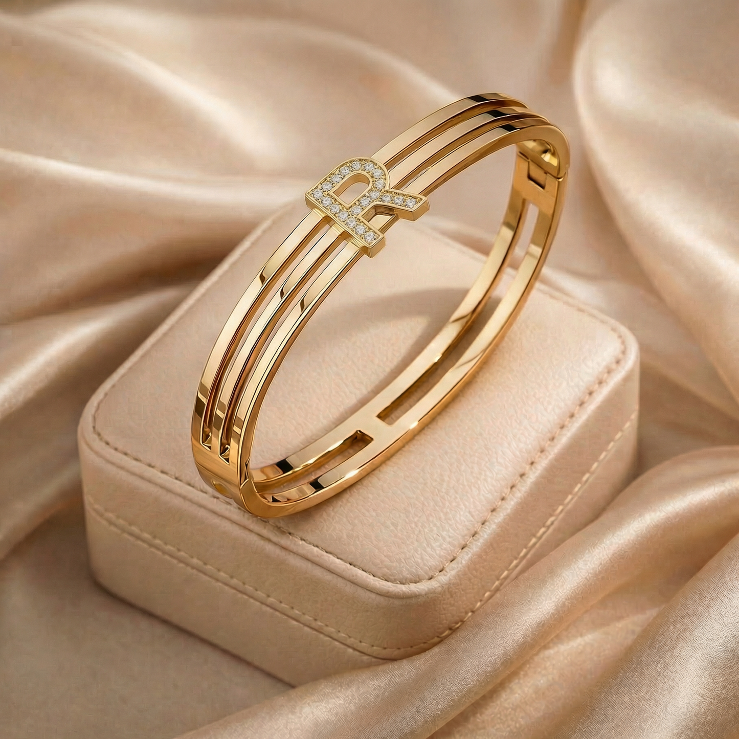 Gold bracelet with 'R' charm on a beige satin background