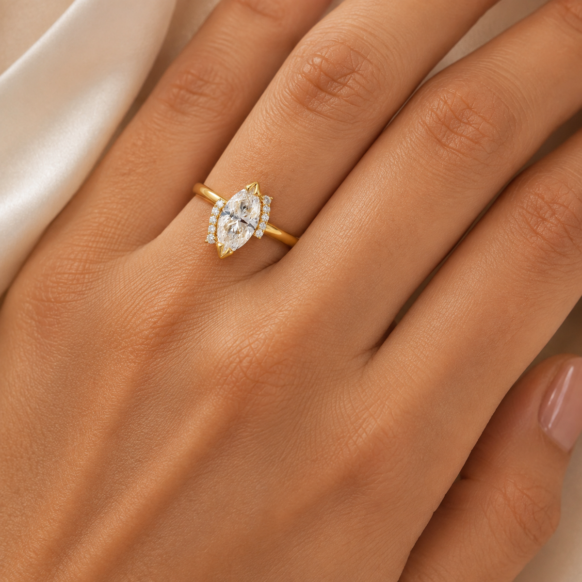 A close-up of a hand wearing a yellow gold ring with a marquise-cut clear center stone and small side stones, set against a soft neutral background.