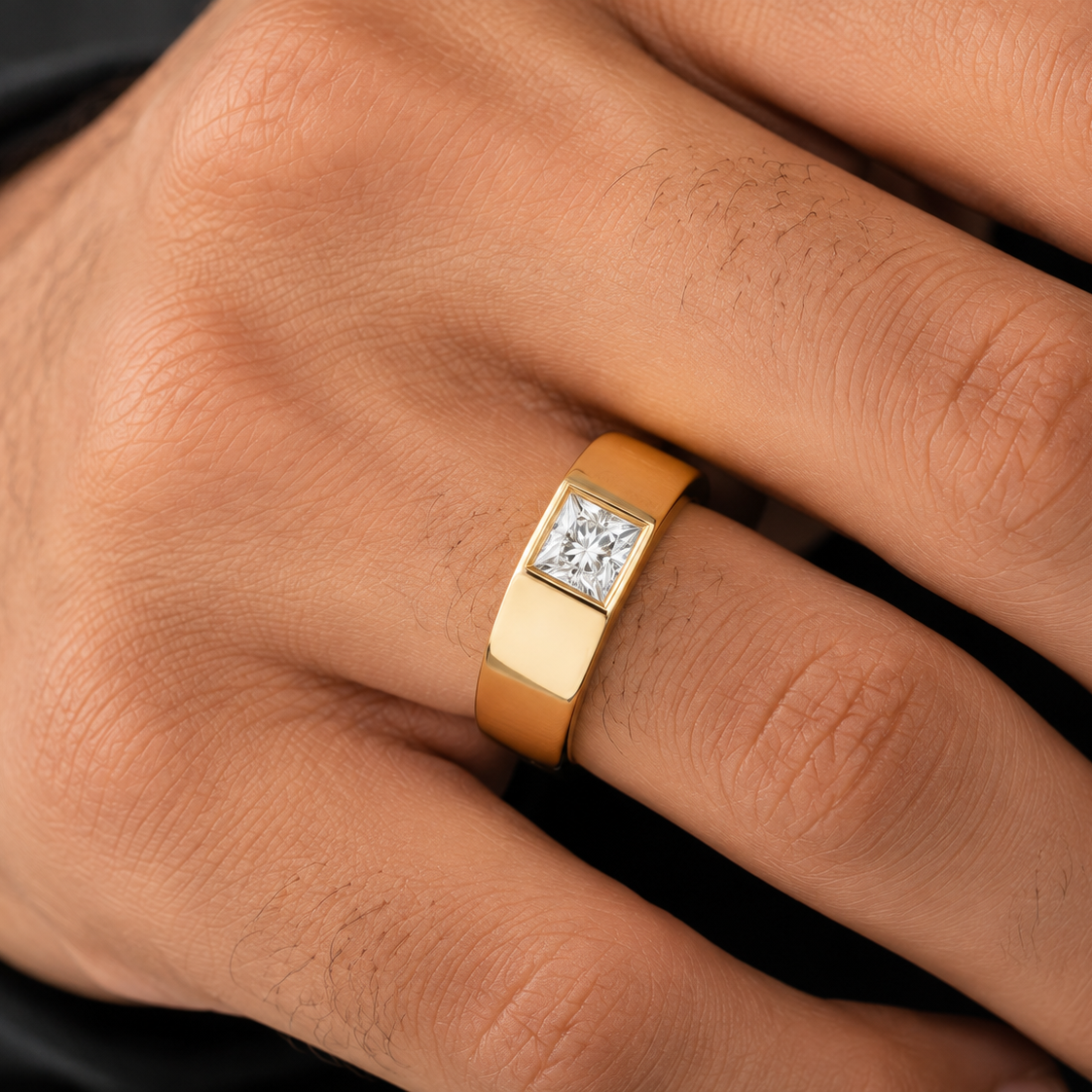 A close-up of a man's hand wearing a gold ring with a square bezel-set diamond.