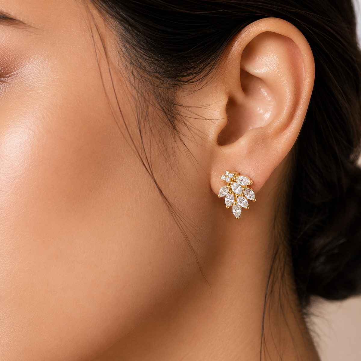 woman's ear wearing a small gold leaf-shaped stud earring set with clear marquise-cut gemstones