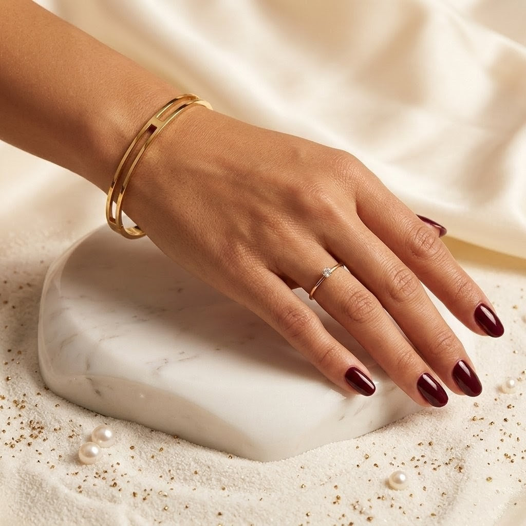 Hand wearing a gold bracelet and ring on a marble surface with pearls.