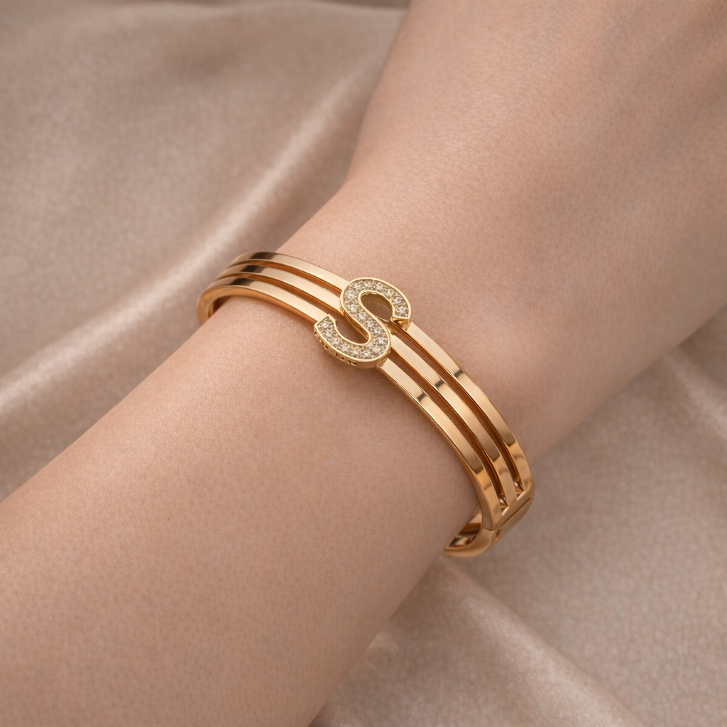 Gold bracelet with a letter 'S' design on a beige fabric background