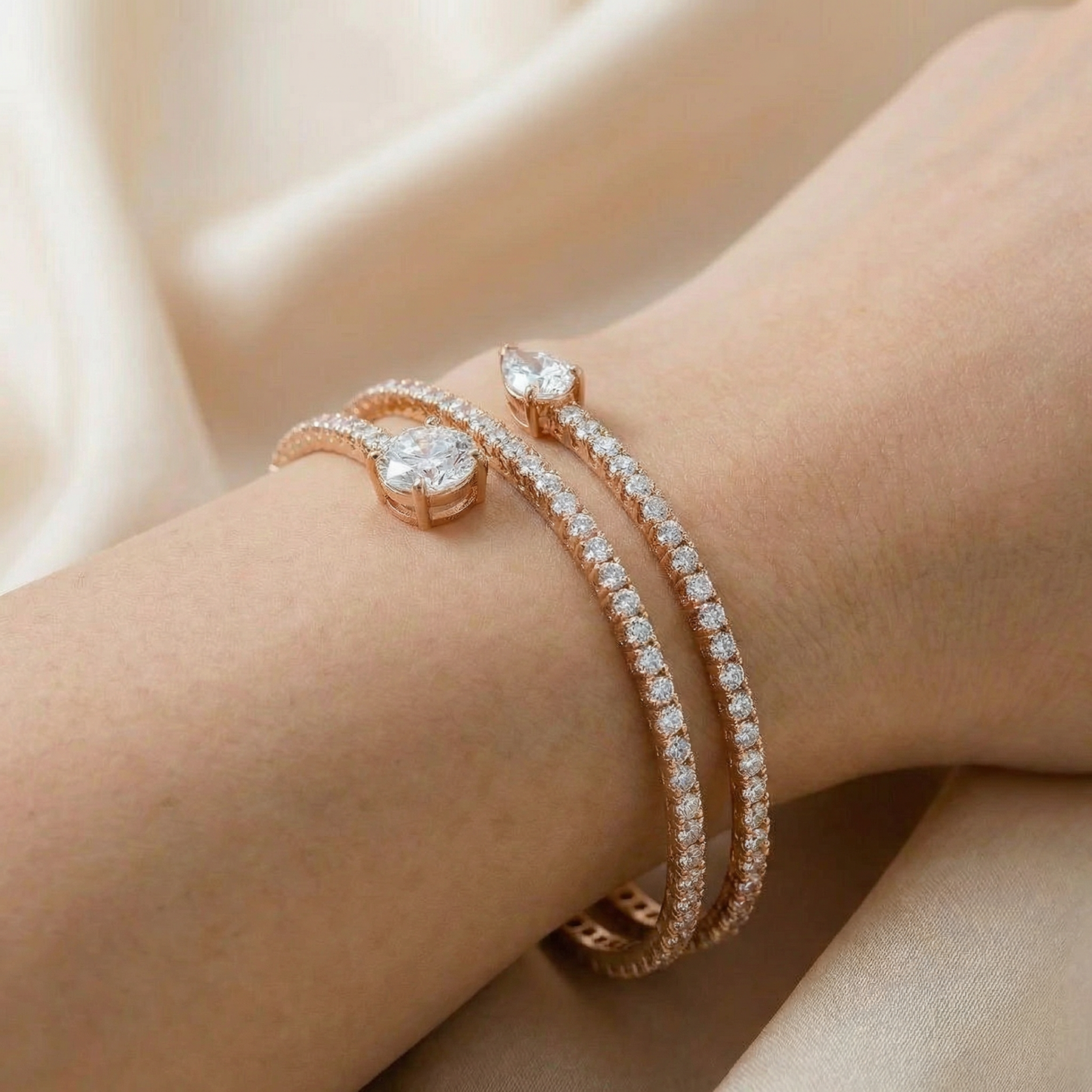 Rose gold bracelet with clear stones on a wrist against a beige fabric background