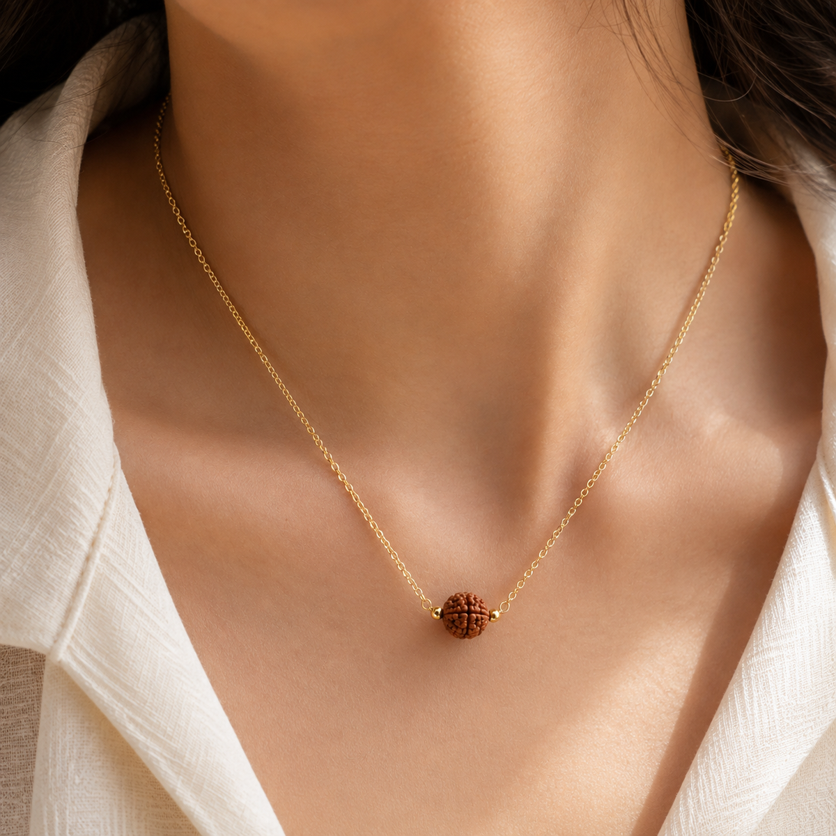 gold chain necklace with a small, textured reddish-brown bead rudraksha pendant 