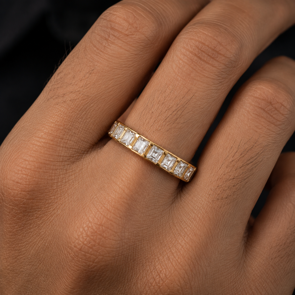 hand wearing a yellow gold eternity ring set with baguette-cut clear diamonds 