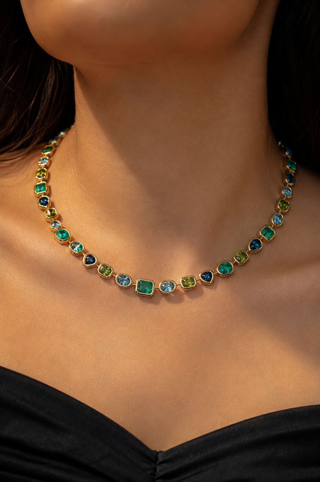 model wearing a gold necklace with multiple small, colorful gemstones in green, blue, and purple settings