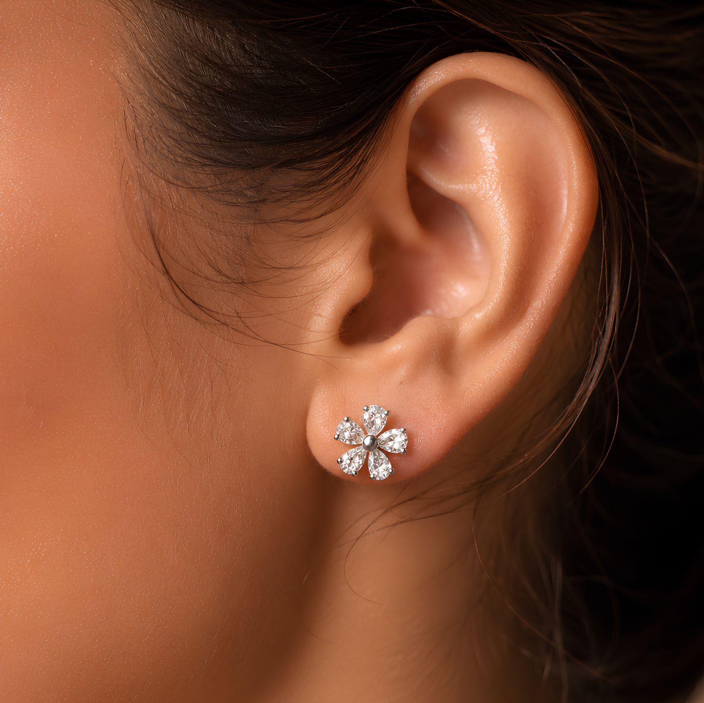 Woman ear wearing a small flower-shaped stud earring with clear sparkling stones in a silver-toned setting.